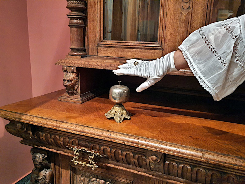 Die antike Tischglocke, die im Stadtmuseum in einer nachgestellten Szenerie zu sehen ist, wurde einst verwendet, um das Personal durch die weiß behandschuhte Hand der Hausherrin anzurufen. Die antike Tischglocke, die im Stadtmuseum in einer nachgestellten Szenerie zu sehen ist, wurde einst verwendet, um das Personal durch die weiß behandschuhte Hand der Hausherrin anzurufen.
